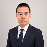 Professional headshot of a man in a navy suit and blue tie against a light gray background.